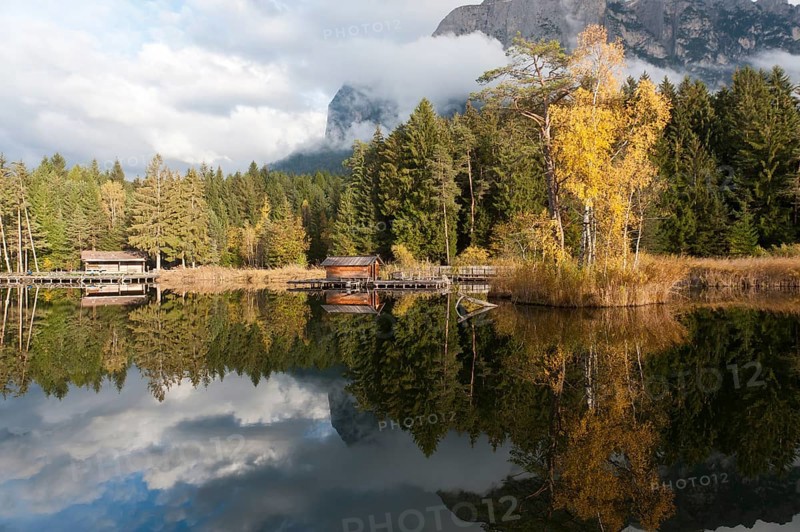 Hut and trees in autumn reflected in the Volser Weiher lake