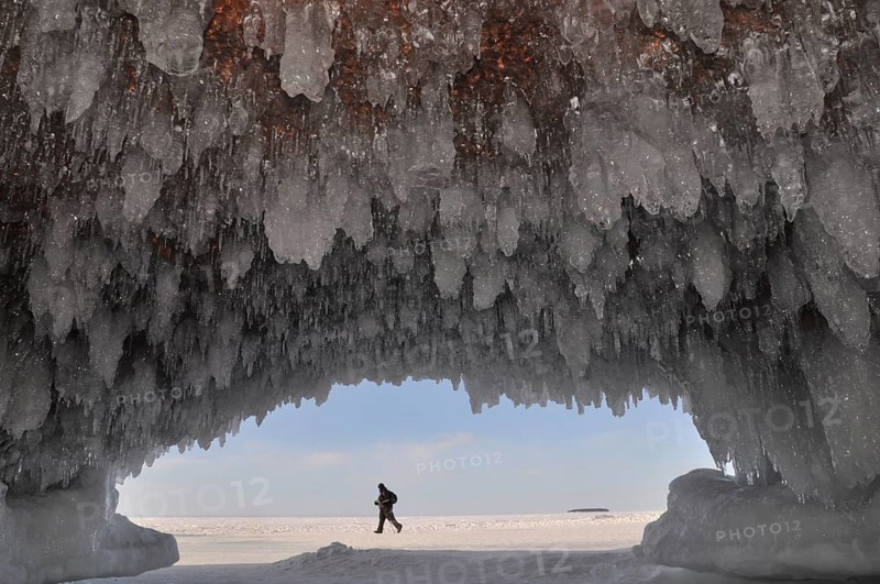 Ice formations and icicles hanging from ceiling in a cave and a man walking on frozen Lake Superior