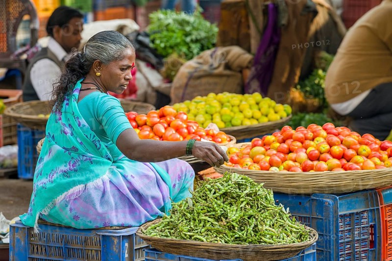 A woman is selling chilis and tomatoes at the weekly vegetable market
