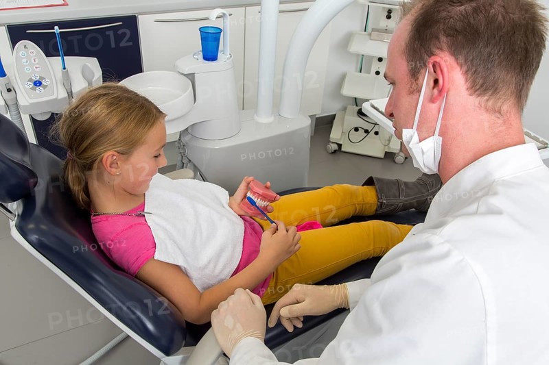 Dentist showing a girl the proper use of a toothbrush