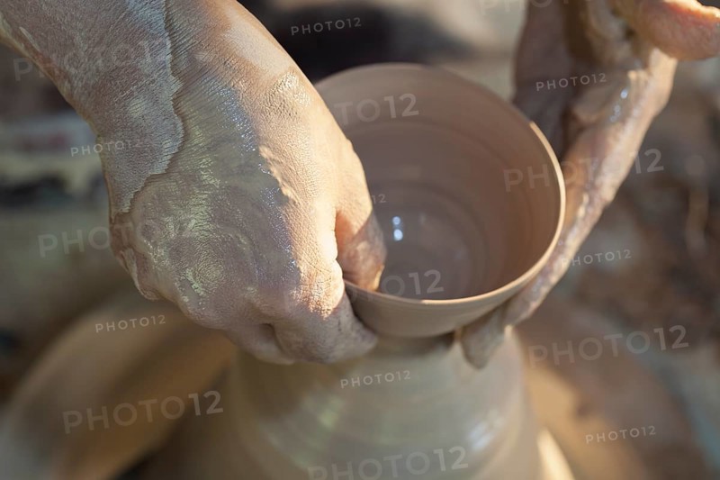 Hands molding a piece of pottery on a wheel head