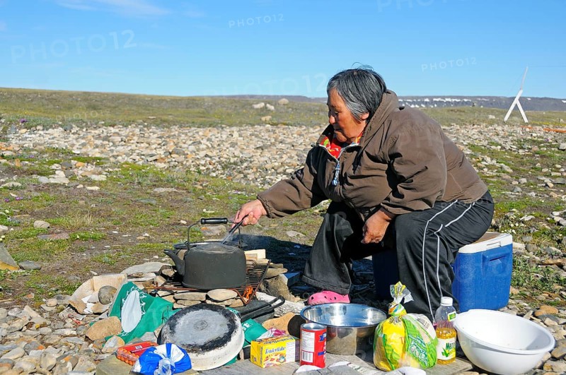 Woman of the Inuit people cooking on a campfire in the tundra