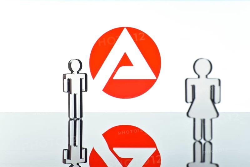Two figures standing in front of the logo of the German employment agency