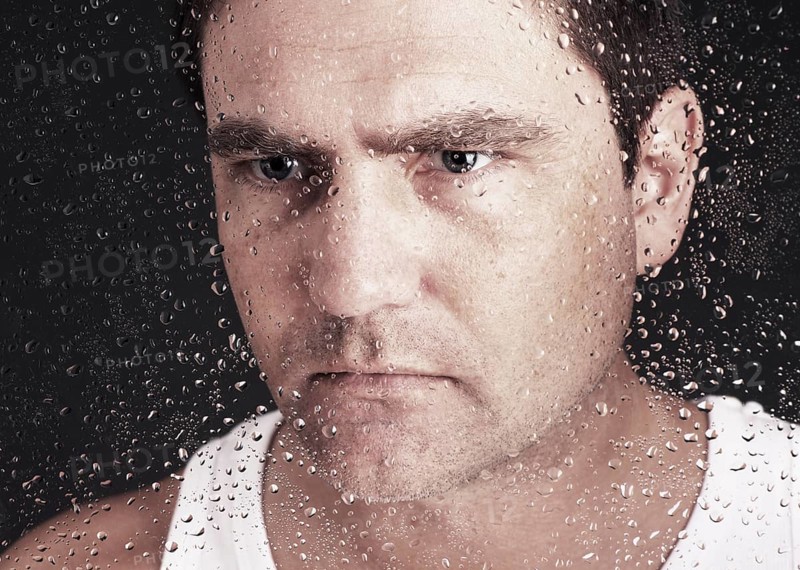 Closeup of pensive man looking through window covered with raindrops
