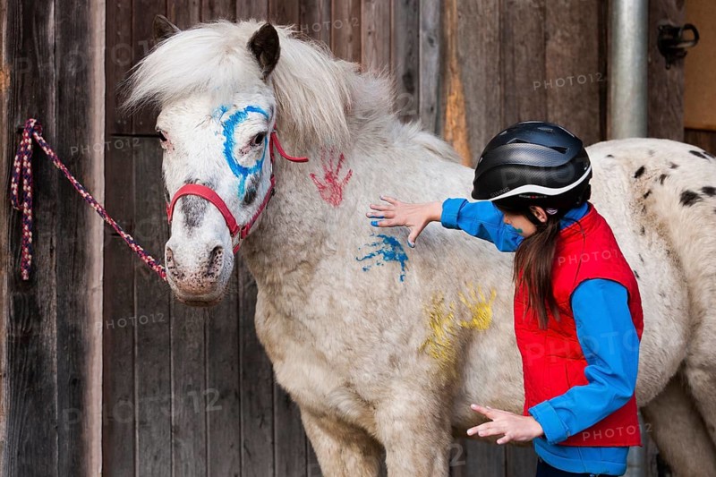 Girl wearing a riding helmet painting a pony with finger paints