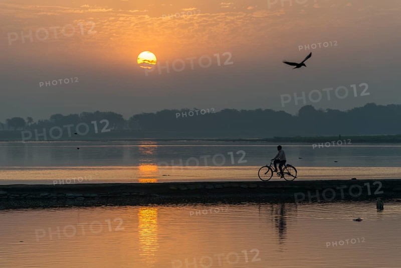 A cyclist crossing the Yamuna river on a dam at sunrise