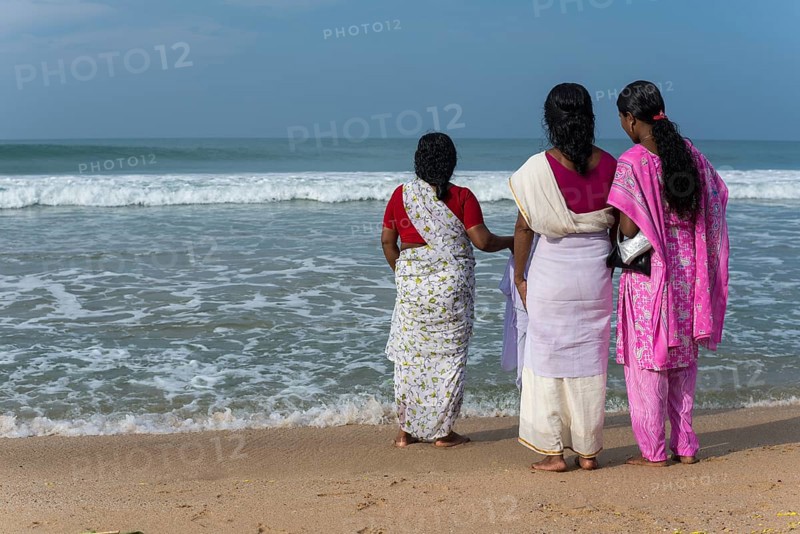 Women standing on the beach facing the sea