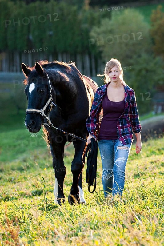 A young woman and a black Hanoverian horse walking on a mountain meadow