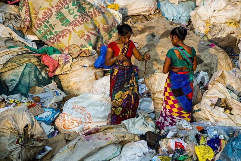 Two women in colorful saris are sorting out garbage for recycling