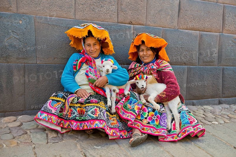 Two Quechua women in traditional dress holding lambs in their arms