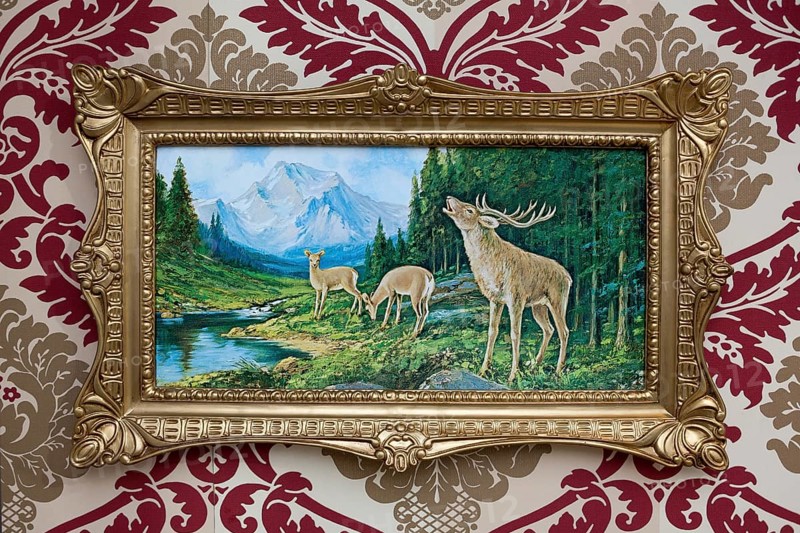 Trashy deer picture in a plastic gold frame on patterned wallpaper