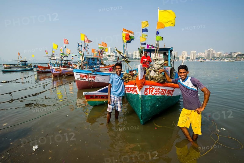 Two fishermen and some fishing boats in front of the skyline of the suburb Churchgate seen across the Back Bay