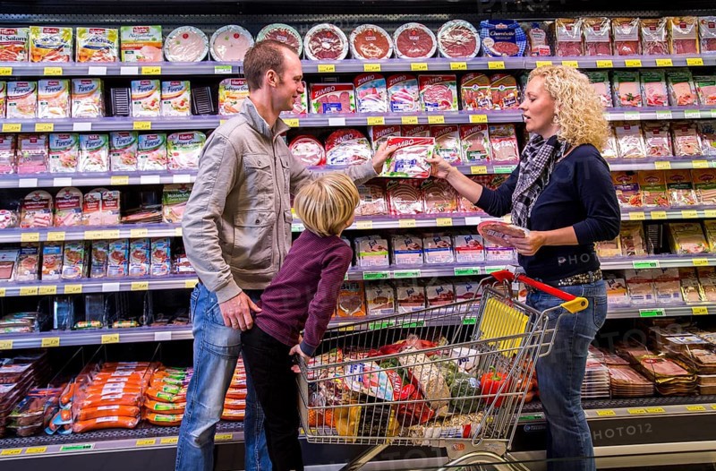 Family shopping with a shopping trolley in the packed meat department of a supermarket