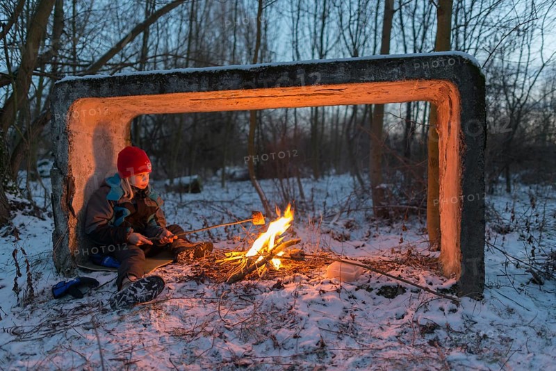 Young boy sitting by the campfire in the snow toasting bread