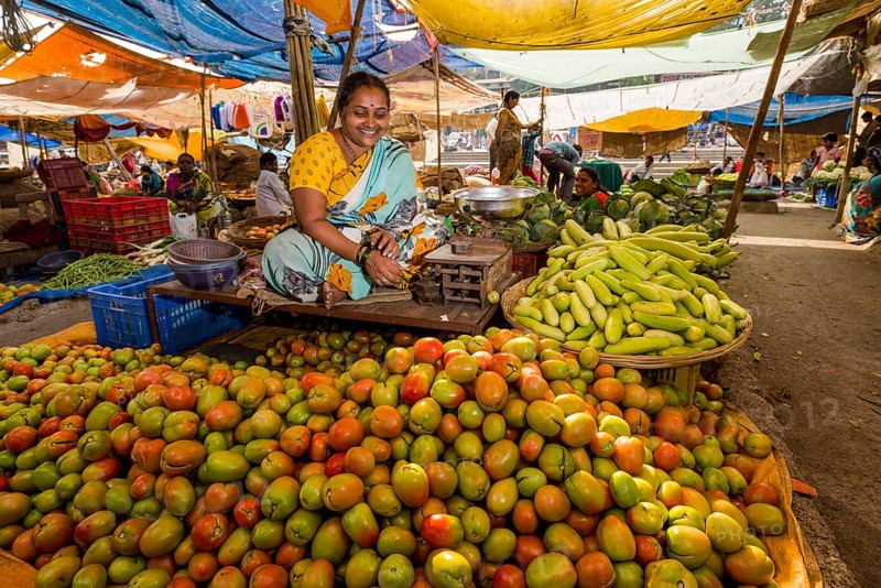 A woman is selling tomatoes and cucumbers at the weekly vegetable market