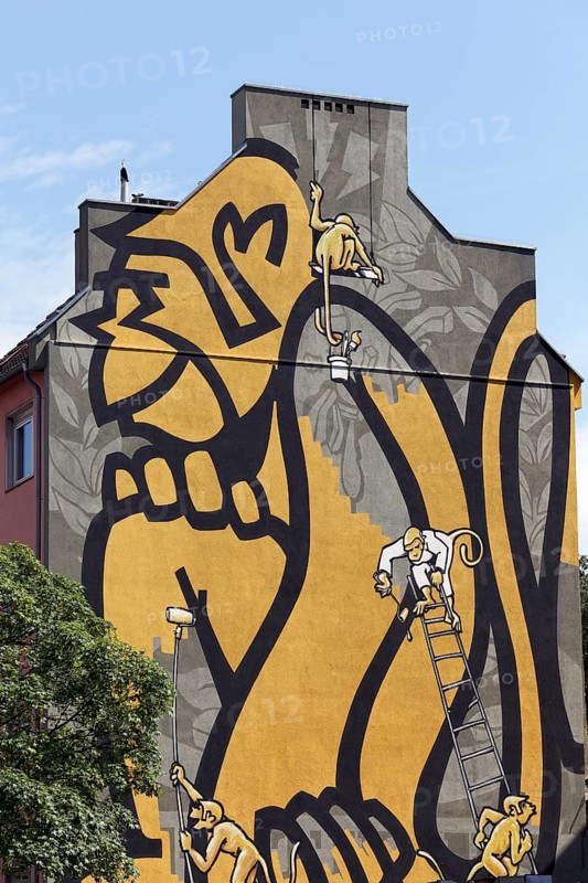 Small monkeys painting a huge monkey on a house wall