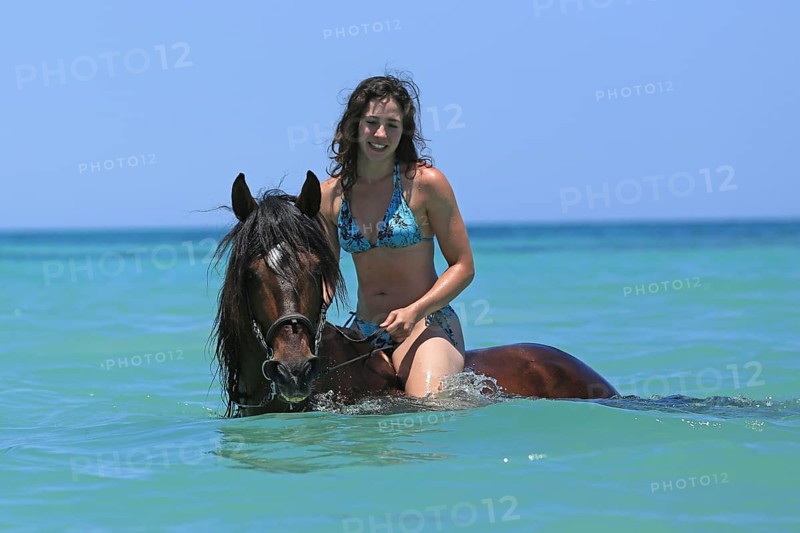 Woman wearing a bikini riding a Barb horse in the sea