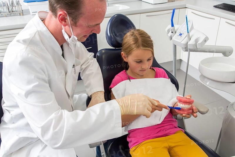 Dentist showing a girl the proper use of a toothbrush