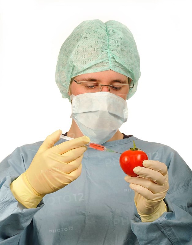 Chemist in sterile scrubs holding a syringe and a tomato