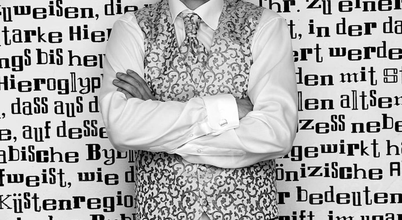 Groom wearing a tie and a waistcoat standing in front of wall with lettering