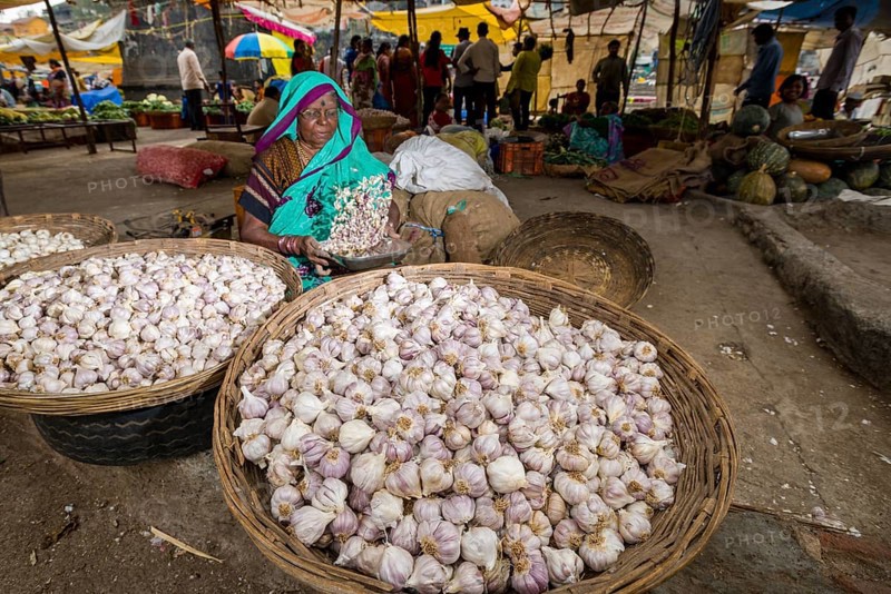 A woman is selling garlic in baskets at the weekly vegetable market