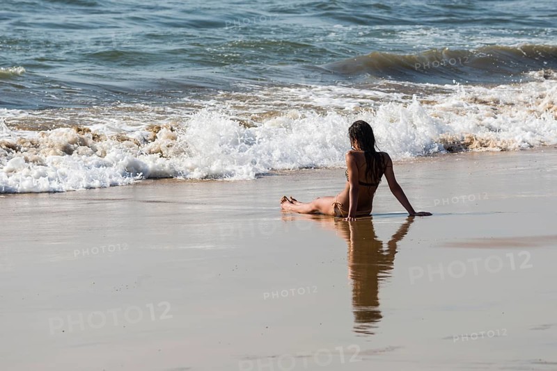 A young woman wearing bikini is sitting in the sand of Anjuna Beach