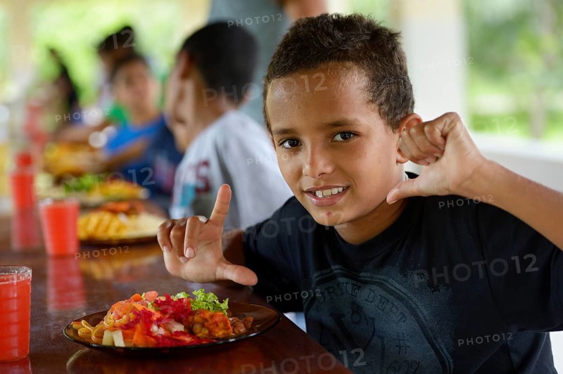 Brazilian boy in front of a full plate of food at the table with other children in a social project for street children