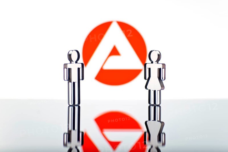 Two figures standing in front of the logo of the German employment agency