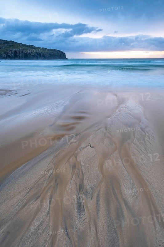 Water flows via bizarre structures on the sandy beach into the sea