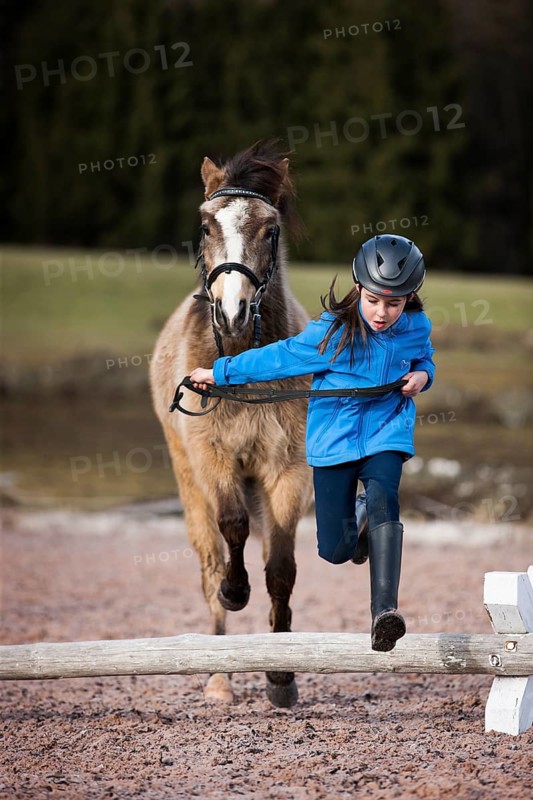 Girl wearing a riding helmet jumping over an obstacle with a pony