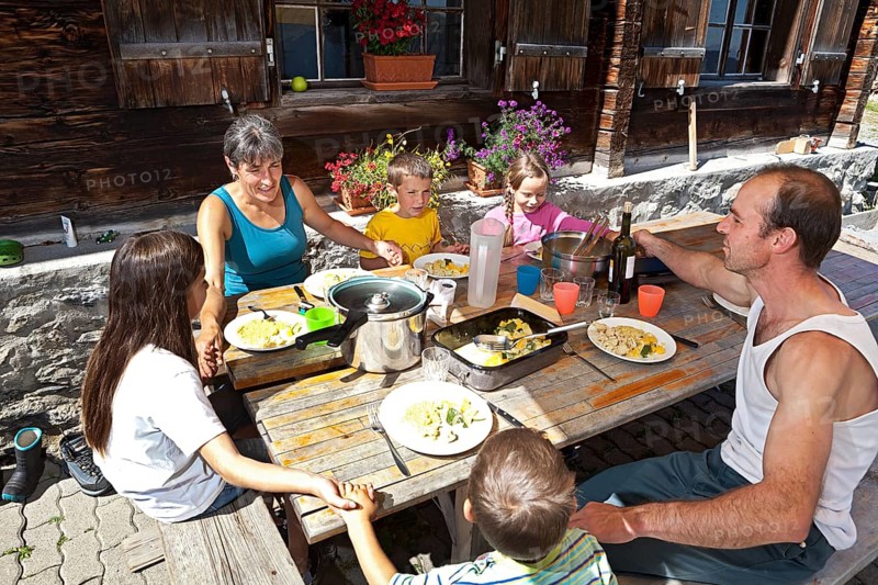 Family holding hands before lunching together in front of a mountain chalet