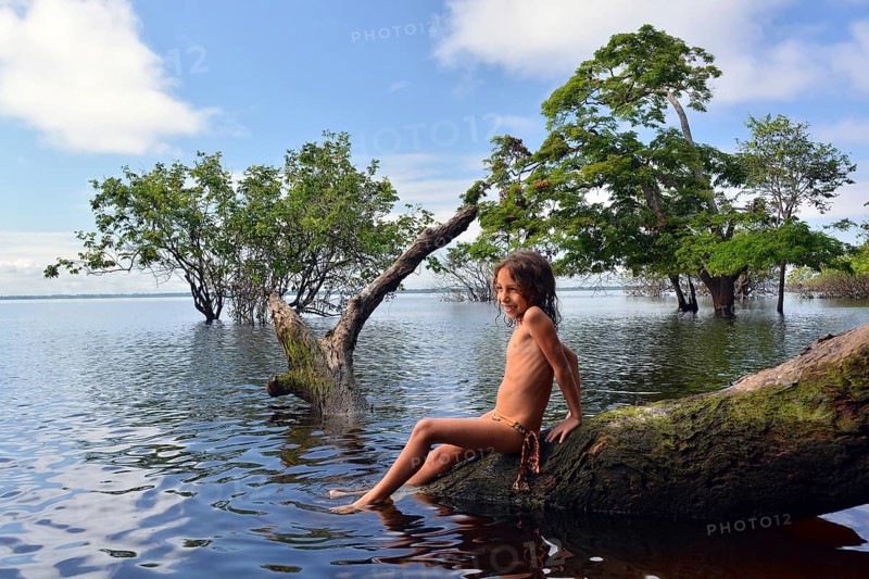 Girl sitting on a tree trunk of a giant rainforest tree on the banks of the Amazon and Rio Solimoes