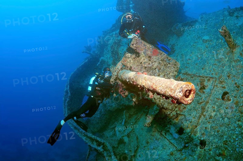 Scuba divers looking at anti-aircraft gun on the stern of the shipwreck 'SS Thistlegorm'