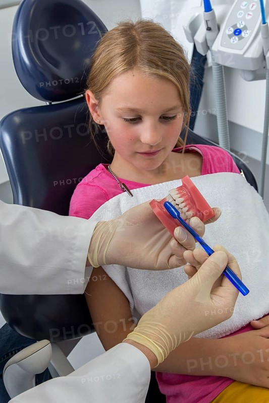Dentist showing a girl the proper use of a toothbrush