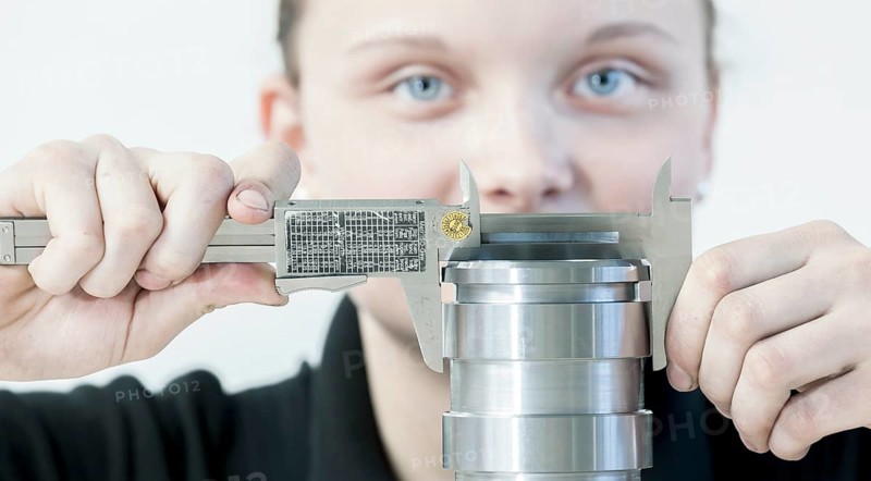 A female cutting machine operator trainee is measuring a casing with a caliper