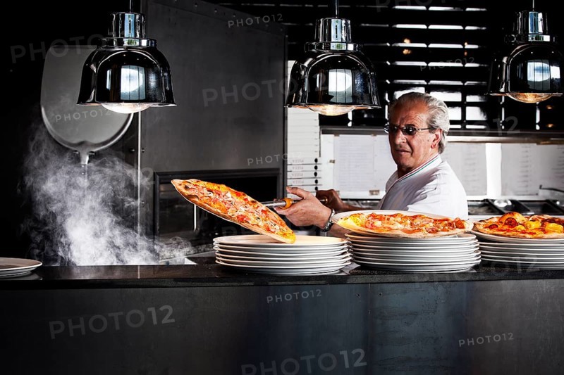Pizza baker taking the finished pizza out of the oven with a pizza shovel
