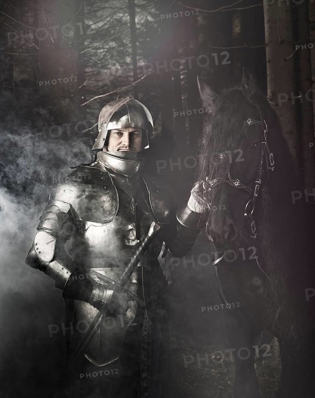 Knight wearing armour standing beside his horse in the woods