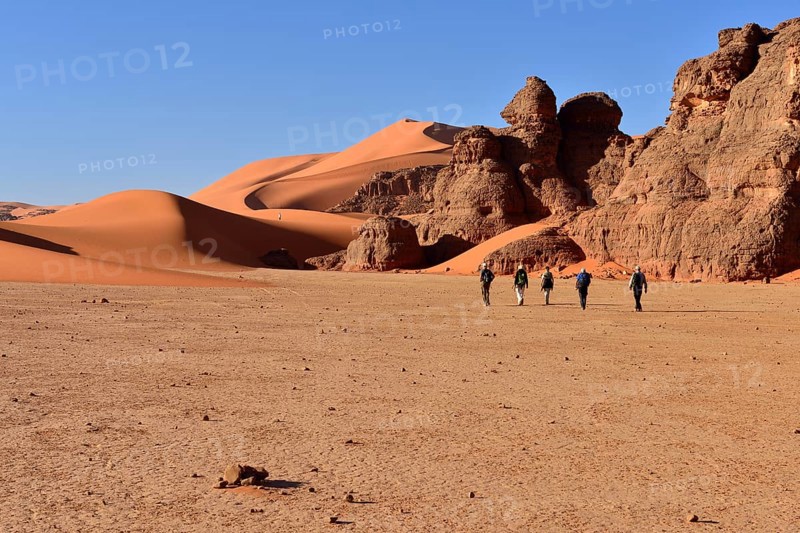 People hiking between rocks and sand dunes of Tin Merzouga