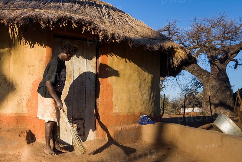 Woman sweeping in front of adobe house