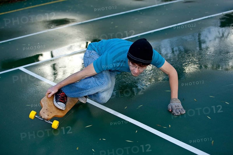Teenage boy skating with his longboard in a tennis court yard