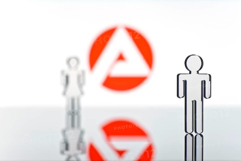 Two figures standing in front of the logo of the German employment agency