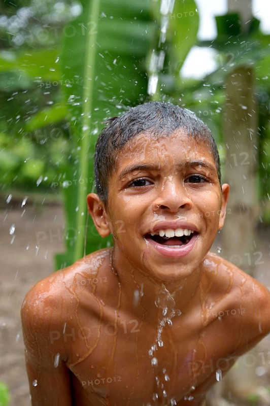 Brazilian boy holding his head in a stream of water and laughing