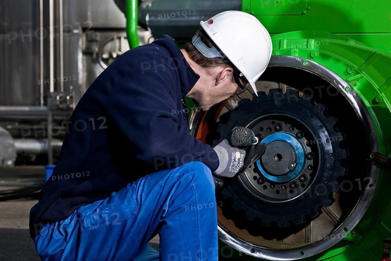 Technician attaching the connecting gear-wheel of an electric generator with an impact wrench