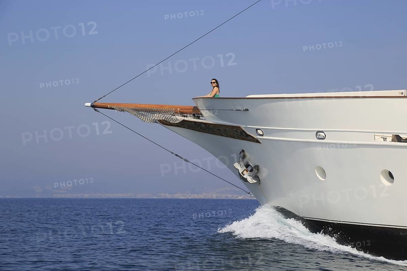 Young woman standing at the bow of a historic yacht and overlooking the sea