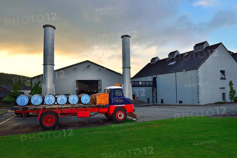 Old lorry loaded with whiskey barrels parked in front of a distillery