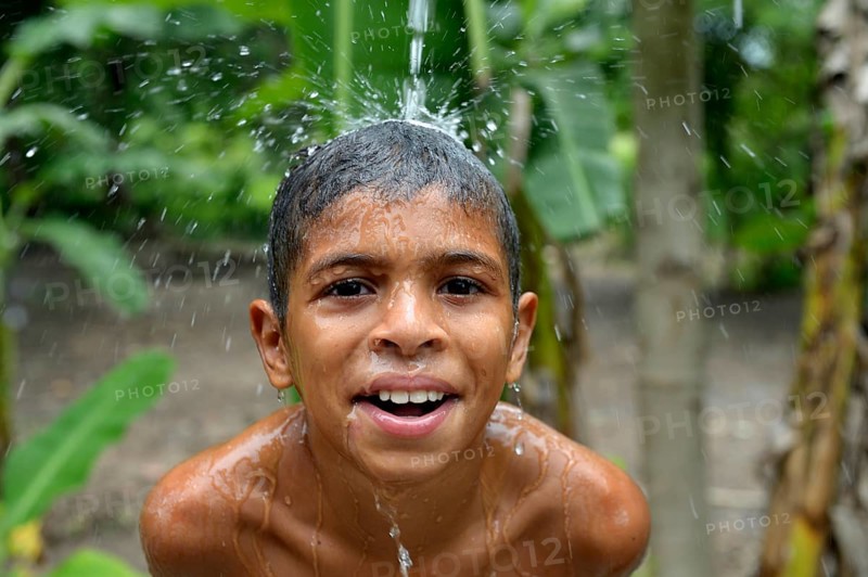Brazilian boy holding his head in a stream of water and laughing