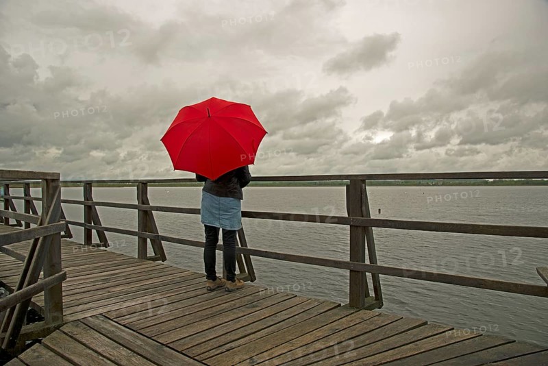 Woman holding a red umbrella on a wharf on Federsee lake