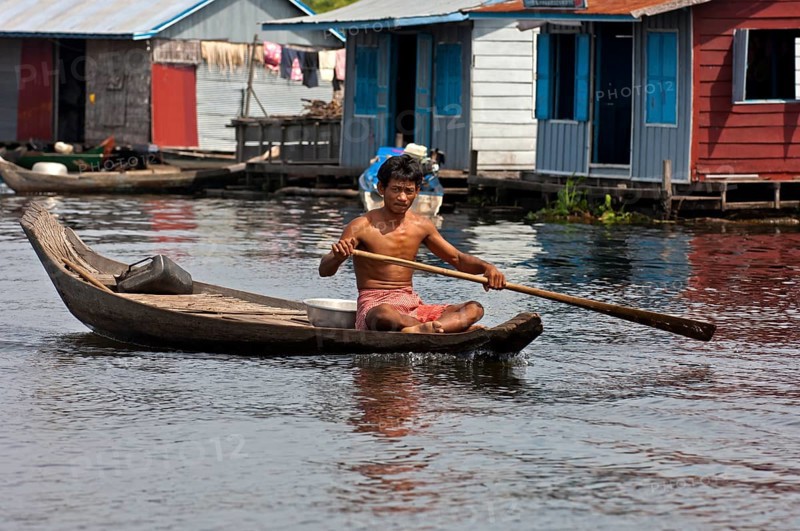 Man paddling a boat near a floating village on Tonle Sap Lake