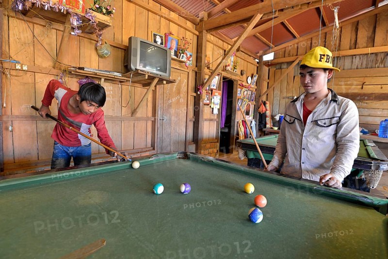 Two Cambodian youths playing pool billiards in a simple wooden hut