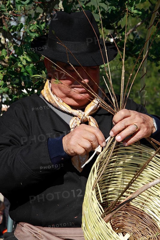 Elderly man in traditional costume making a basket at a traditional handicraft fair